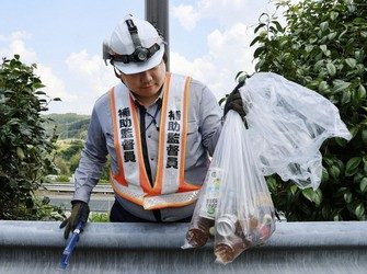 Работник держит прозрачный мусорный пакет с бутылками, наполненными мочой, и другим мусором, собранным во время уборки на парковке Бёбудзан скоростной автомагистрали Тюо в городе Мидзунами, префектура Гифу, 12 июня 2026 года. (Киодо)