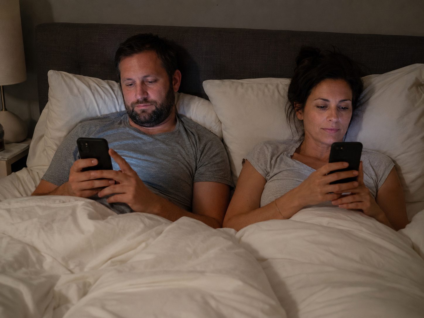 Two people in bed using their phones.